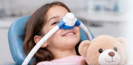 Niña sonriendo con mascarilla nasal de óxido nitroso mientras abraza un oso de peluche